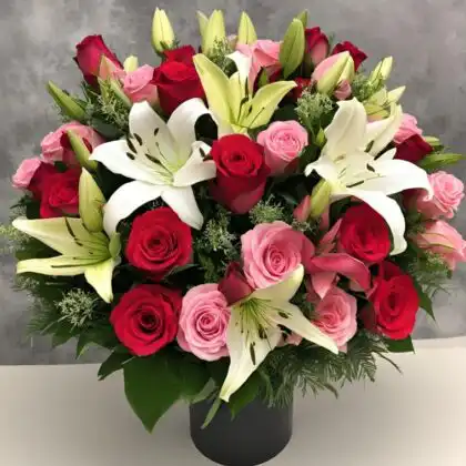 Fresh red and pink roses and lily bouquet arranged with white oriental lilies in a modern black vase.
