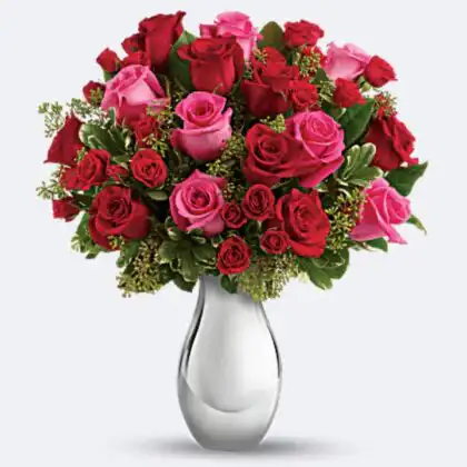 A beautiful red and pink roses bouquet arranged with fresh green leaves in a stylish vase.